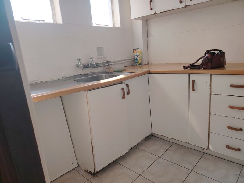 A dated kitchen featuring laminate countertops, built-in cabinetry, and a stainless steel sink, requiring cosmetic updates and repairs to the cabinetry and wall finishes.