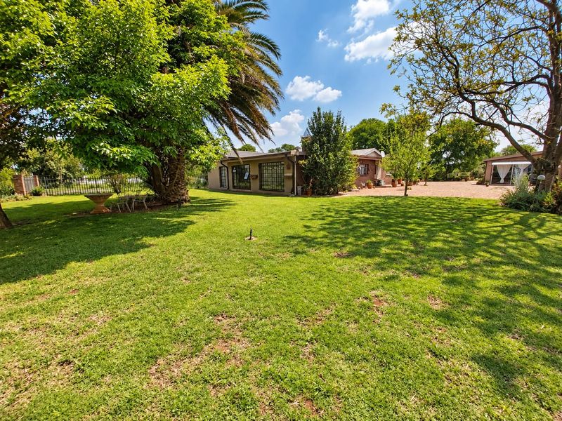 A spacious, well-maintained garden featuring mature trees, a lush lawn, and a gravel driveway leading to the rear of the property.
