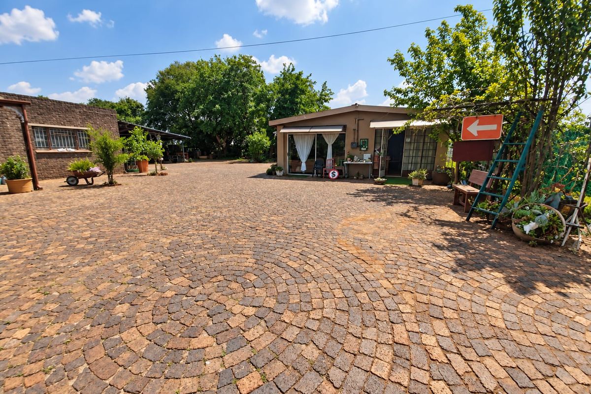 Spacious rear courtyard featuring extensive cobblestone paving, brick outbuildings, and a covered patio area with sliding glass doors.