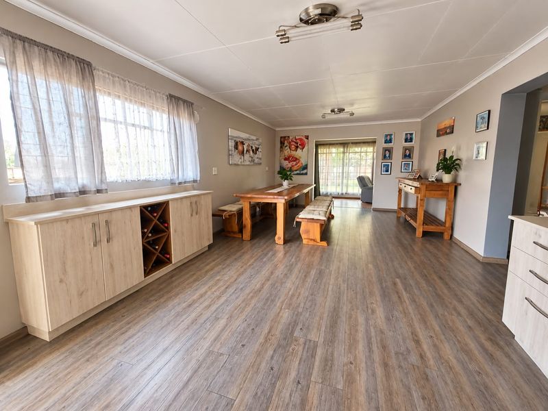 Spacious dining area featuring modern laminate flooring, a built-in sideboard with integrated wine storage, and natural light through large windows and sliding doors.