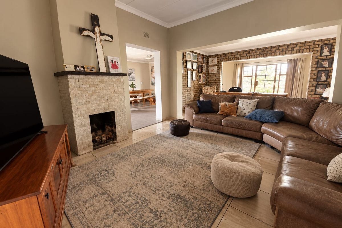 Spacious living room featuring a stone-clad fireplace, exposed brick feature wall, and neutral tiled flooring, creating a warm and inviting atmosphere.
