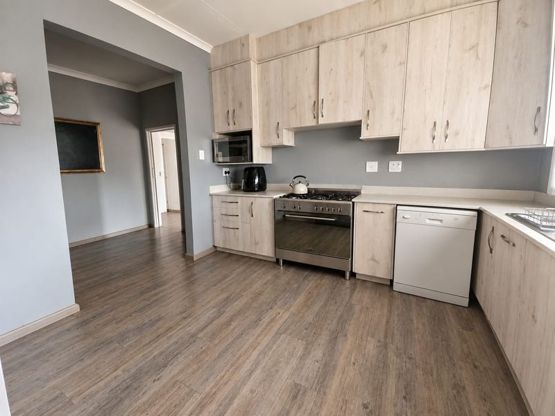 Modern kitchen featuring light wood-finish cabinetry, stone countertops, a gas stove with oven, and durable laminate flooring, seamlessly connected to the adjacent living area.