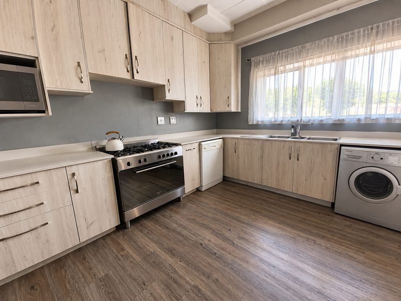 Modern kitchen featuring light wood-grain cabinetry, laminate flooring, stainless steel gas stove, built-in microwave, and a double sink with a window view.