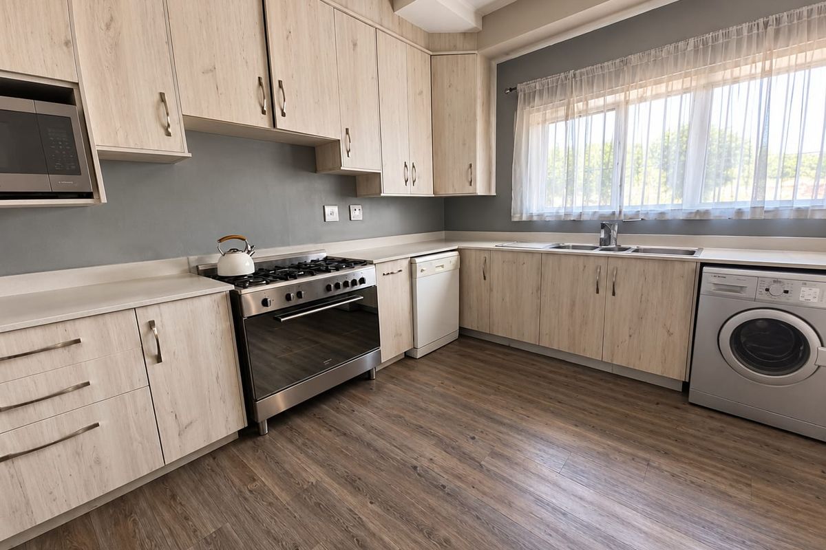 Modern kitchen featuring light wood-grain cabinetry, laminate flooring, stainless steel gas stove, built-in microwave, and a double sink with a window view.