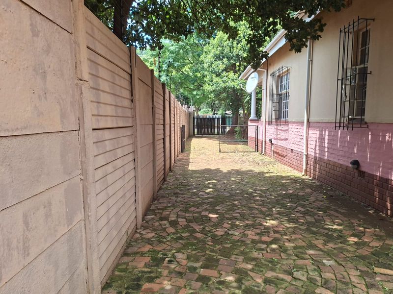 A side exterior walkway featuring a brick paved path, precast concrete boundary wall, and security-fitted windows along the side of the house.