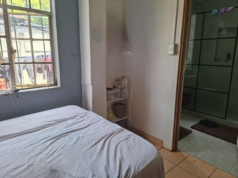 Bedroom featuring tiled flooring, a steel-framed window, and direct access to an en-suite bathroom, requiring cosmetic updates to the walls and finishes.