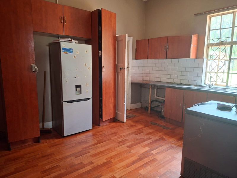 Kitchen featuring wooden cabinetry, subway tile backsplash, and laminate flooring. The space requires cosmetic updates and repairs to cabinetry and plumbing fixtures.