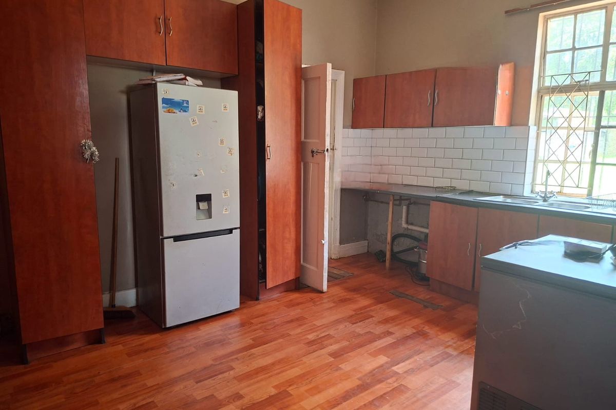 Kitchen featuring wooden cabinetry, subway tile backsplash, and laminate flooring. The space requires cosmetic updates and repairs to cabinetry and plumbing fixtures.
