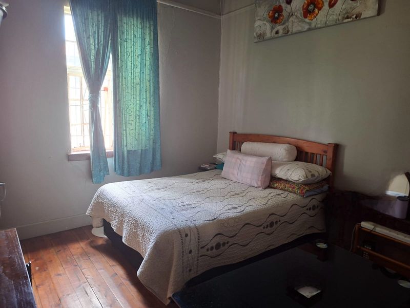 A bedroom featuring original timber flooring and a window with security bars, showing signs of wear on the wall surfaces.