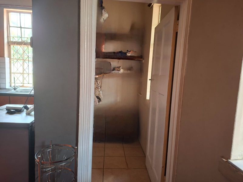 A small scullery or pantry area featuring tiled flooring and built-in shelving, currently showing significant signs of wear and wall staining.