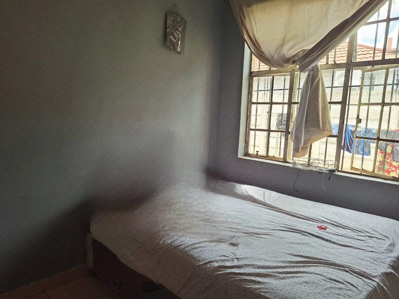 A bedroom featuring a steel-framed window and tiled flooring, requiring cosmetic updates to improve the overall aesthetic and condition.
