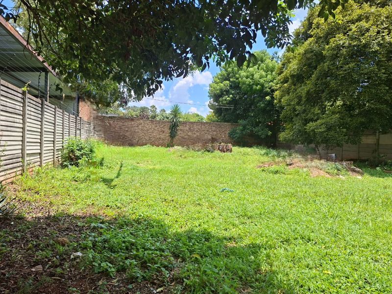 A spacious, private backyard featuring established trees, a brick boundary wall, and secure perimeter fencing, offering significant potential for landscaping.