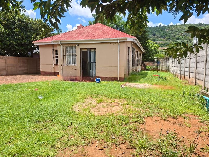 Rear view of the house featuring a red corrugated metal roof, security bars on windows, and a spacious backyard with precast concrete boundary walls.