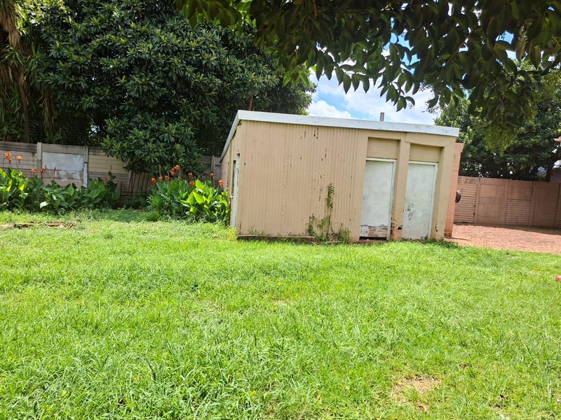 Rear garden area featuring a weathered corrugated metal outbuilding, mature trees, and precast concrete boundary walls.