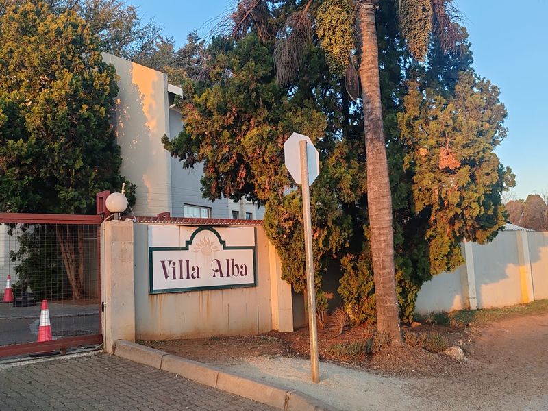 Front entrance view of Villa Alba complex featuring a perimeter wall, security gate, and paved driveway access.