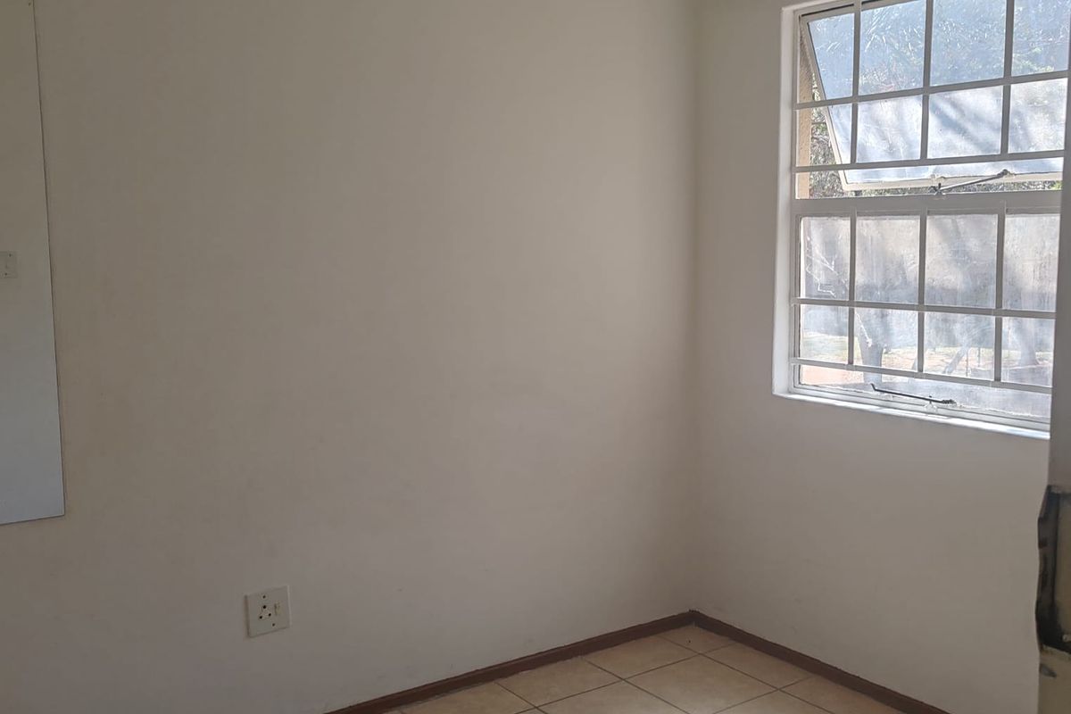 A vacant bedroom featuring neutral tiled flooring, a grid-pattern window, and plain walls, offering a blank canvas for personalization.