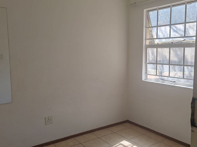 A vacant bedroom featuring neutral tiled flooring, a grid-pattern window, and plain walls, offering a blank canvas for personalization.