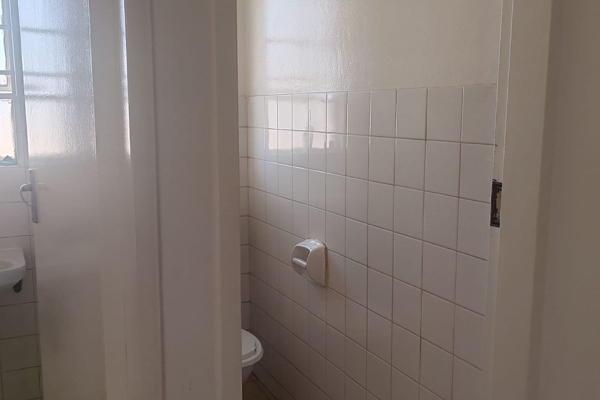 A compact, dated bathroom featuring white wall tiles, tiled flooring, and basic sanitary fixtures, presenting an opportunity for modernization and renovation.