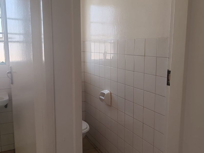 A compact, dated bathroom featuring white wall tiles, tiled flooring, and basic sanitary fixtures, presenting an opportunity for modernization and renovation.