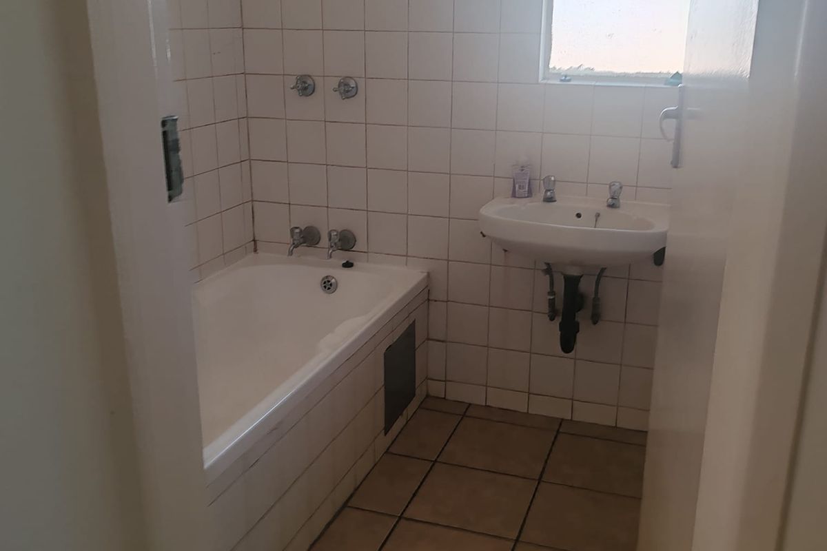 A dated bathroom featuring a built-in bathtub, wall-mounted basin, and tiled finishes, requiring modernization to improve its overall aesthetic and functionality.