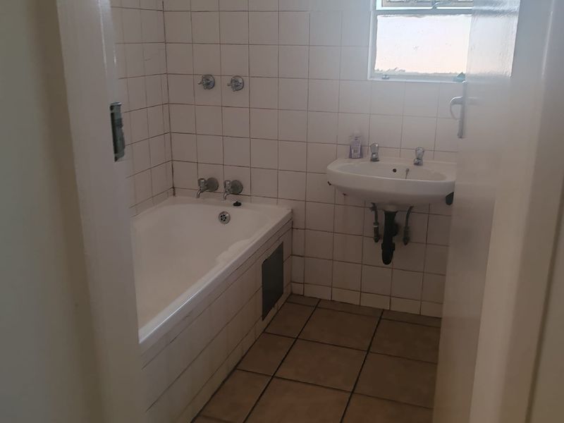 A dated bathroom featuring a built-in bathtub, wall-mounted basin, and tiled finishes, requiring modernization to improve its overall aesthetic and functionality.