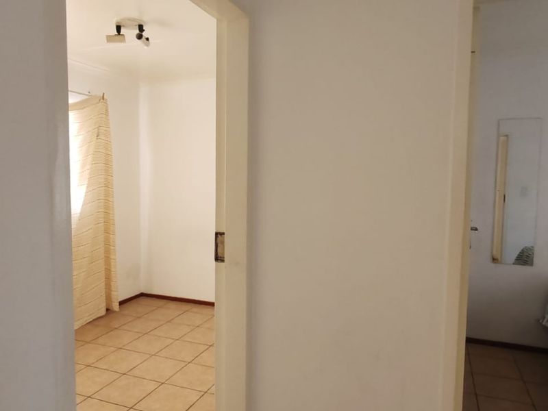 A view from a hallway looking into an empty bedroom with tiled flooring and basic lighting fixtures.