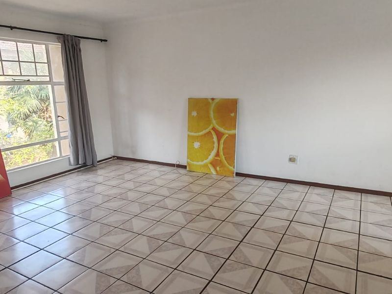 A spacious, empty living area featuring tiled flooring and large windows, providing a blank canvas for interior design and personalization.
