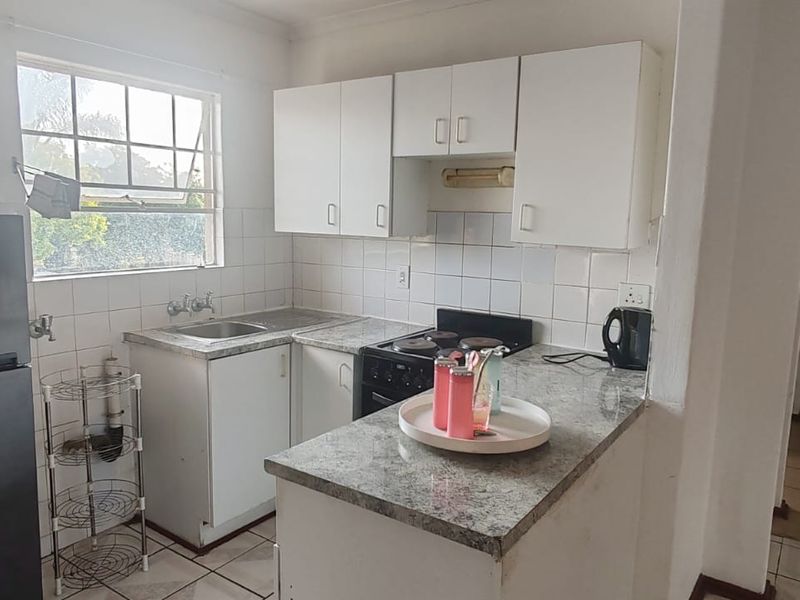 A functional kitchen featuring laminate countertops, tiled backsplash, and white cabinetry, with a view into the adjacent hallway.