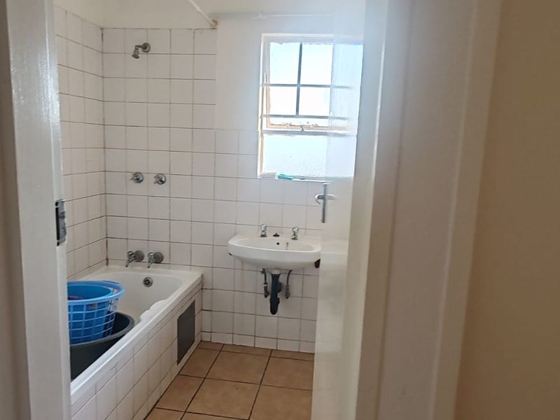A dated bathroom featuring a bathtub with shower head, wall-mounted basin, and tiled finishes throughout, offering potential for a modern renovation.