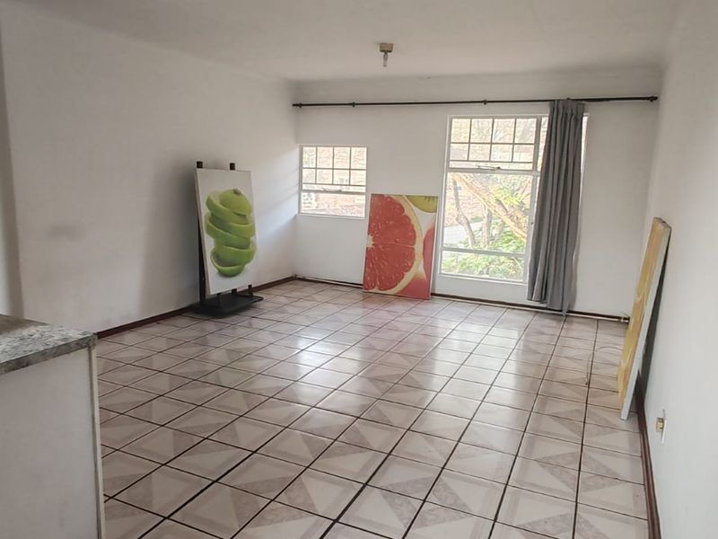 An open-plan living and kitchen area featuring tiled flooring, neutral walls, and large windows, offering a blank canvas for interior design.