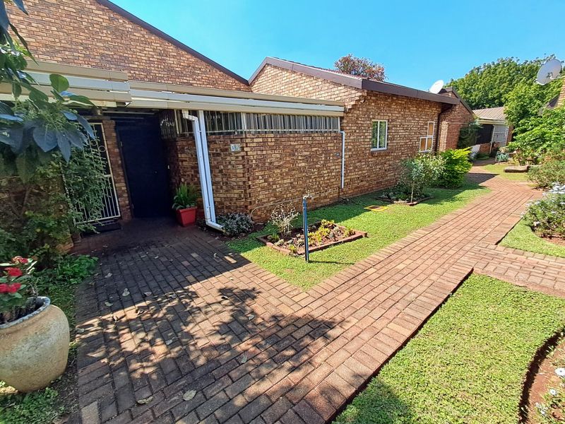 A well-maintained townhouse exterior featuring a face brick facade, paved walkway, and a covered entrance area with established garden surroundings.