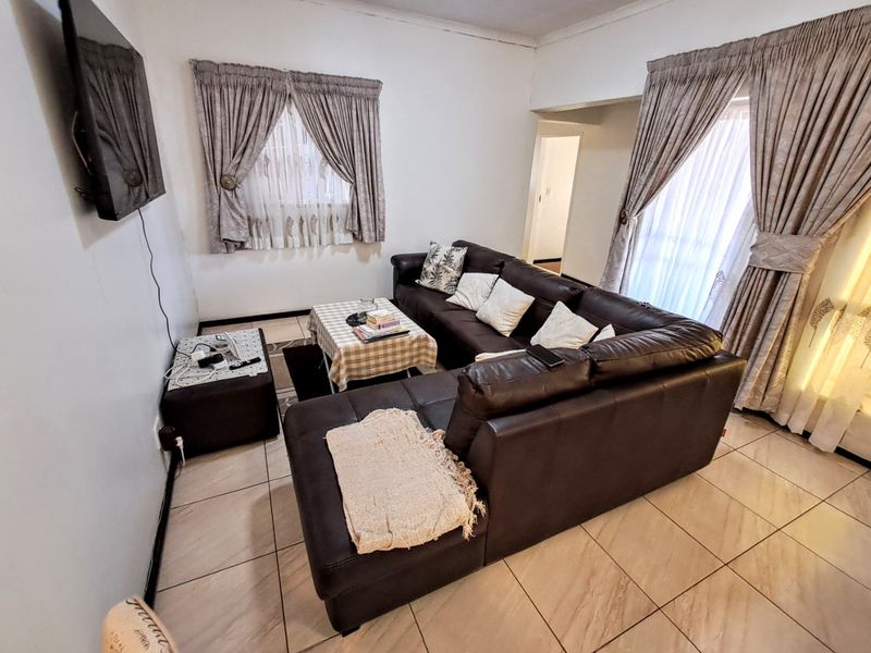 A living room featuring tiled flooring and large windows with curtain rails, providing a functional space for relaxation.