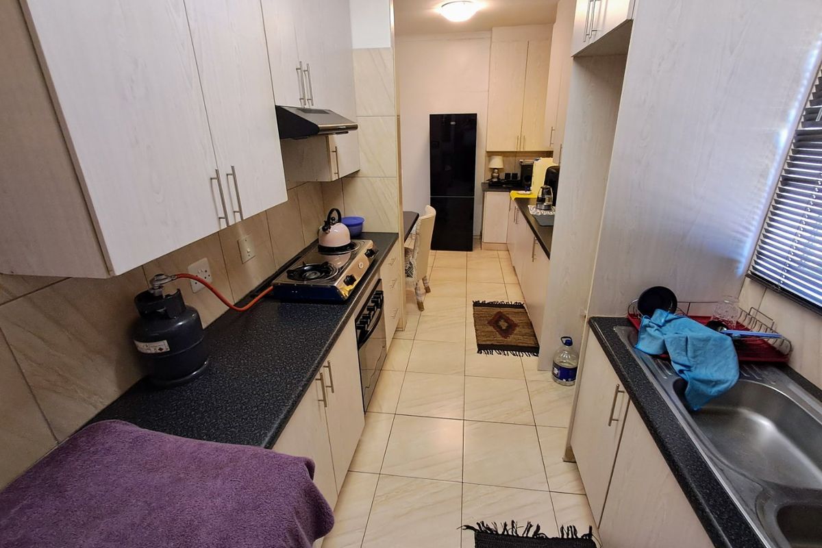 A functional galley-style kitchen featuring light-toned cabinetry, dark laminate countertops, a gas hob, and tiled flooring throughout.
