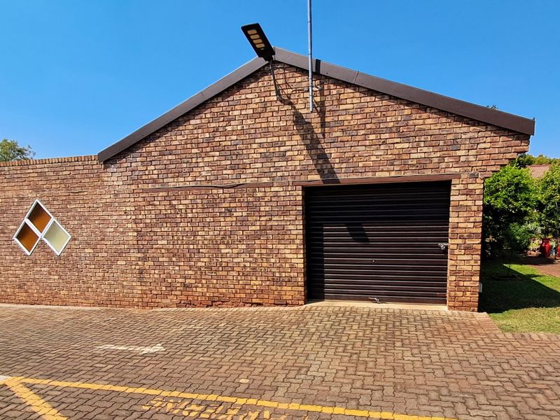 A brick-faced townhouse garage featuring a roller shutter door, a unique diamond-shaped window, and a paved driveway area.