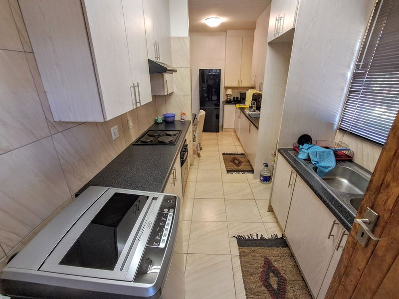 A functional galley-style kitchen featuring light-toned cabinetry, dark laminate countertops, an electric hob, and tiled finishes throughout.