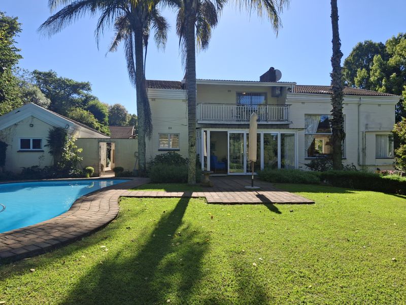 Rear view of the property featuring a swimming pool, landscaped garden, paved patio area, and a balcony overlooking the backyard.