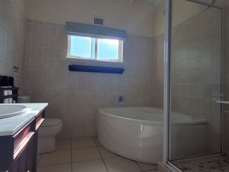 A functional bathroom featuring a corner bathtub, separate shower enclosure, vanity with basin, and neutral wall and floor tiling.