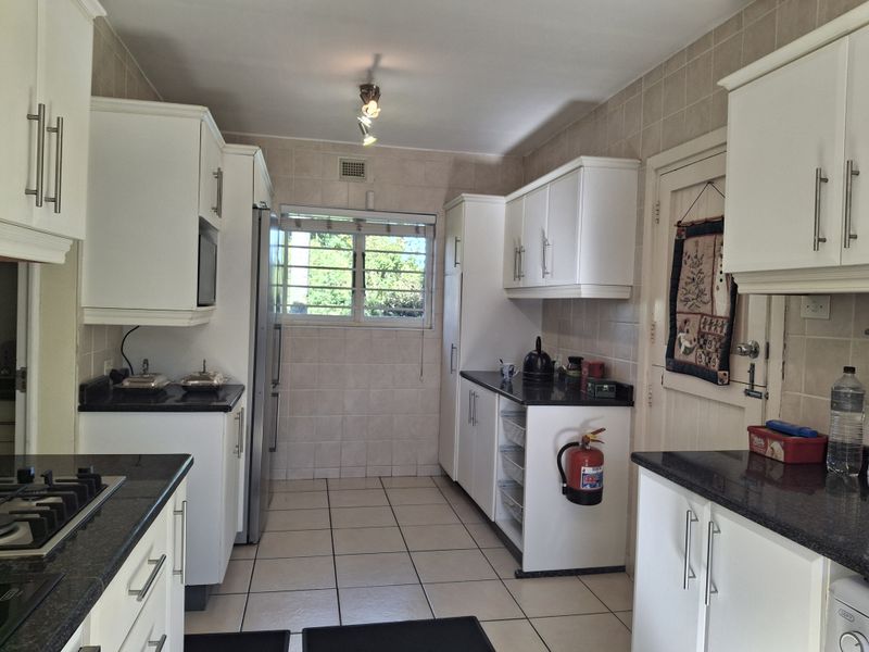 A functional kitchen featuring white cabinetry, dark granite countertops, a gas hob, and tiled finishes throughout.