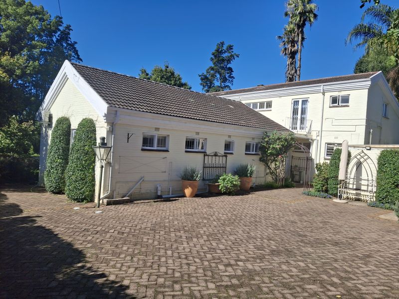 Rear view of the property featuring a paved courtyard, painted brick exterior, tiled roof, and a small upper-level balcony.