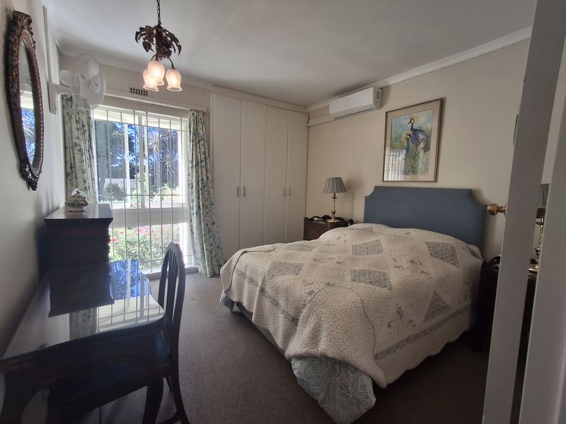 A carpeted bedroom featuring built-in cupboards, a split-system air conditioner, and a sliding glass door with security bars providing access to the garden.