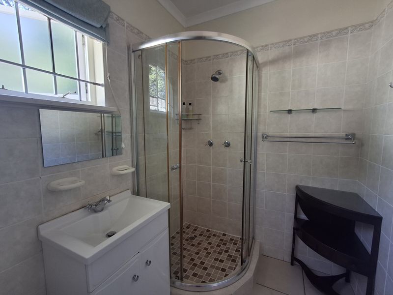A functional bathroom featuring a curved glass shower enclosure, vanity basin, and neutral wall tiling with integrated storage fixtures.