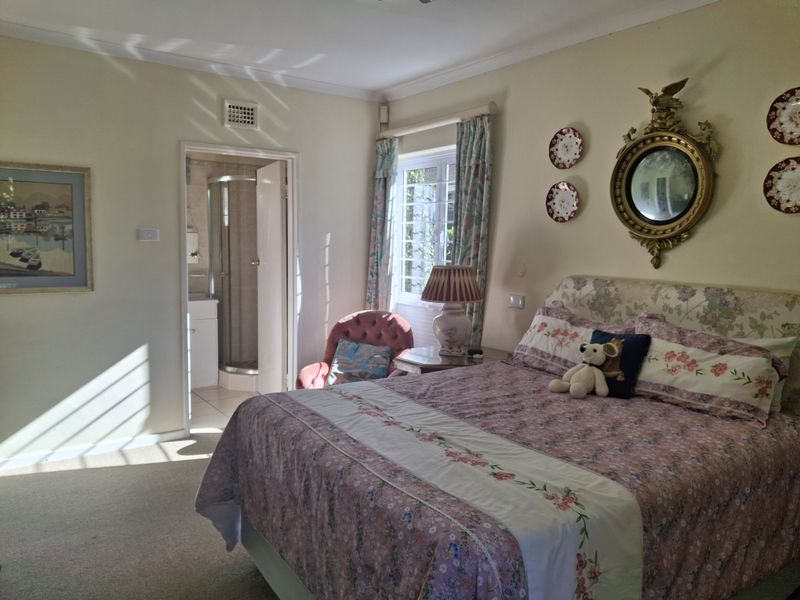 A carpeted bedroom featuring an en-suite bathroom, natural light through a casement window, and decorative cornice detailing.