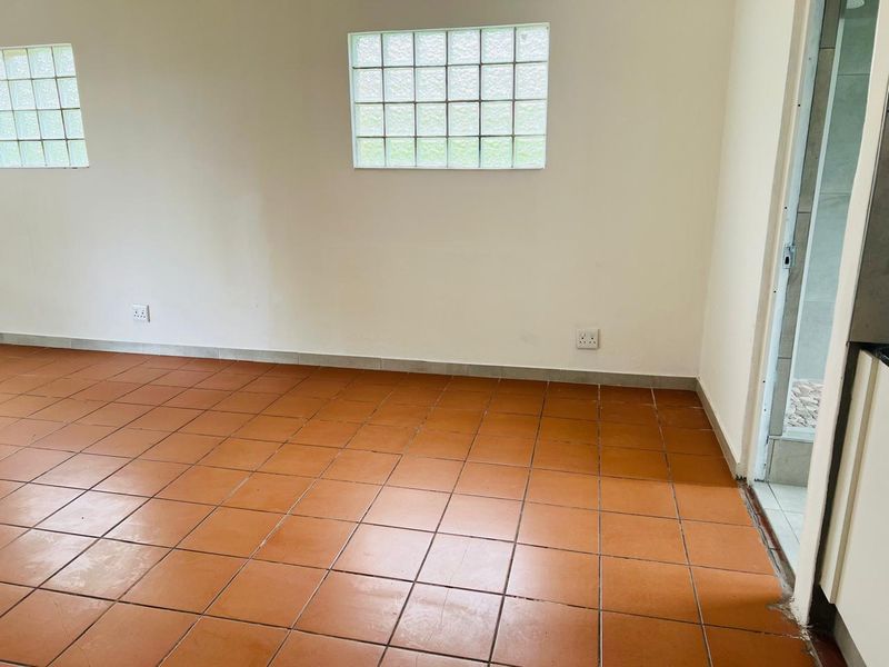 An empty living area featuring terracotta-style ceramic floor tiles and glass block windows, providing a blank canvas for interior design updates.