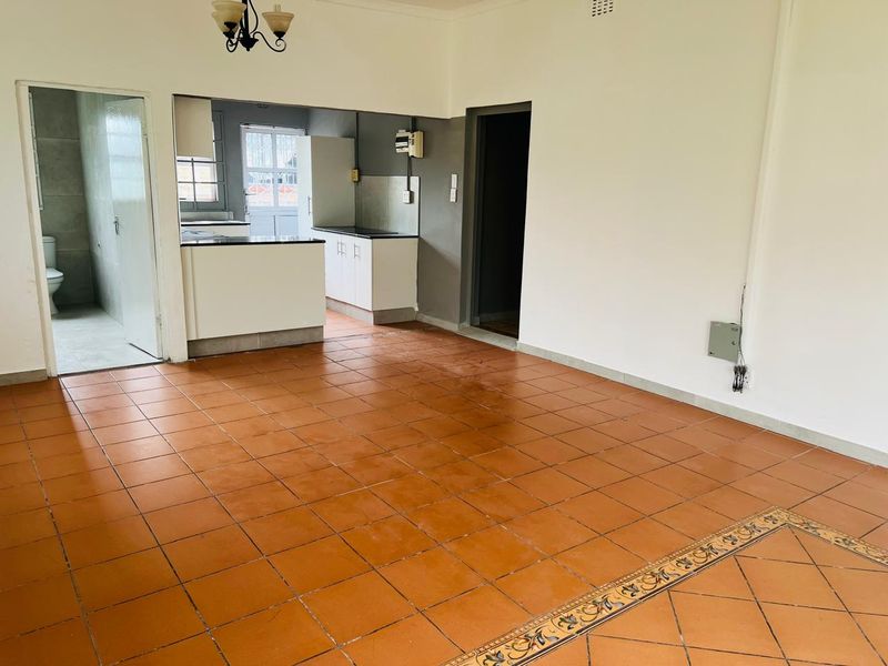Open plan living area featuring terracotta tiled flooring, leading into a functional kitchen space with built-in cabinetry and granite countertops.