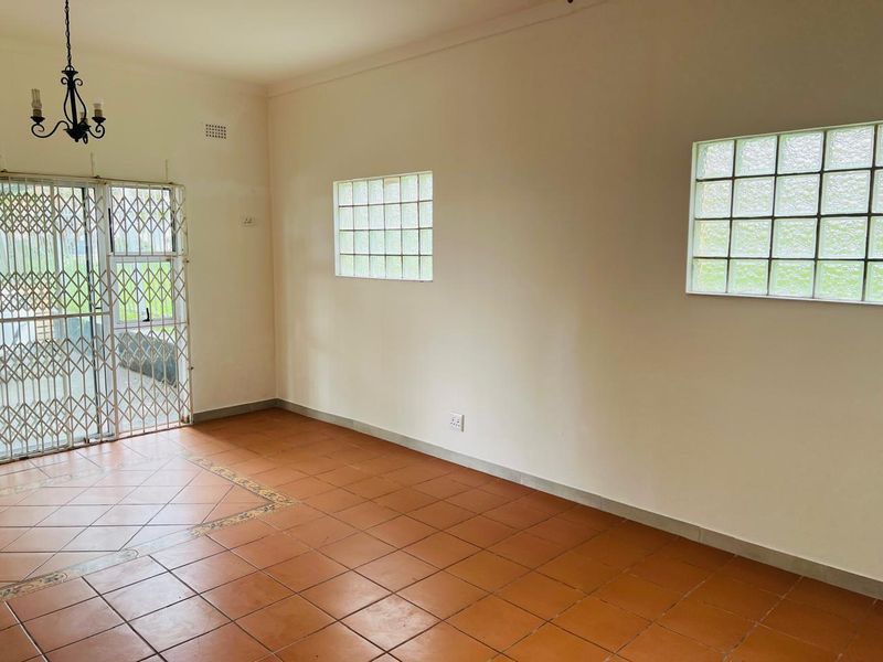 An empty living room featuring ceramic tile flooring, glass block windows, and a security gate leading to the exterior.