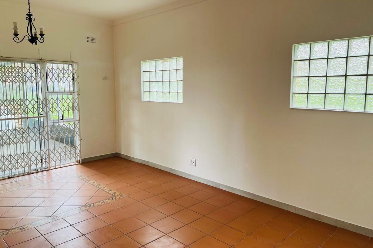 An empty living room featuring ceramic tile flooring, glass block windows, and a security gate leading to the exterior.
