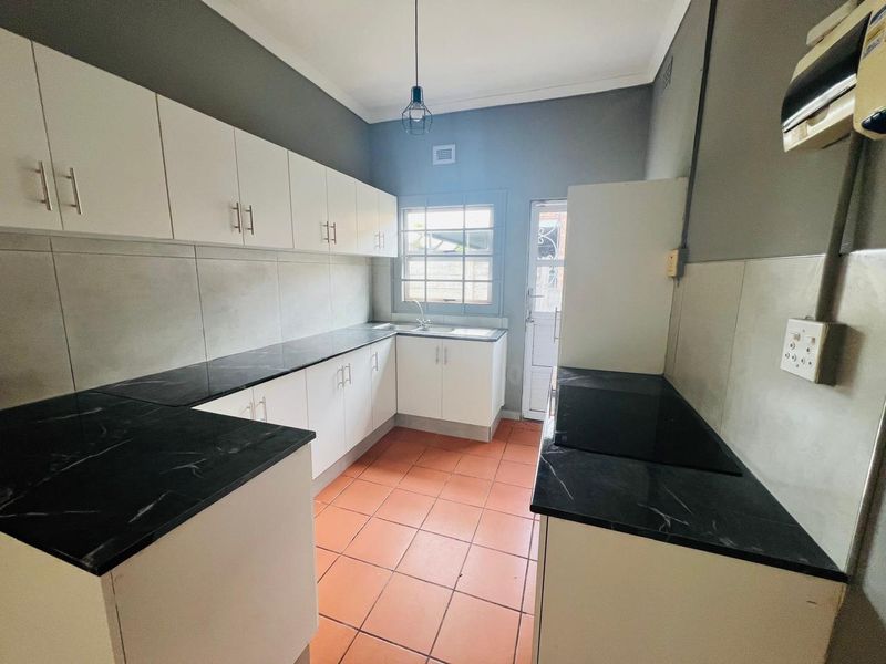 A clean, functional kitchen featuring white cabinetry, dark marble-look countertops, tiled backsplash, and ceramic floor tiles with direct access to the exterior.