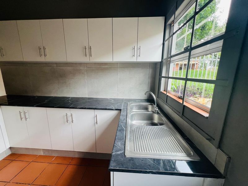 A clean, functional kitchen area featuring white cabinetry, dark marble-effect countertops, a stainless steel double sink, and terracotta floor tiles.