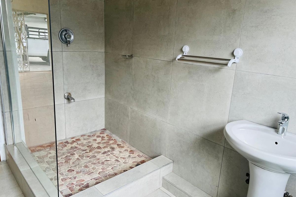 A modern bathroom featuring a walk-in shower with a pebble tile floor, glass screen, and a white pedestal basin.