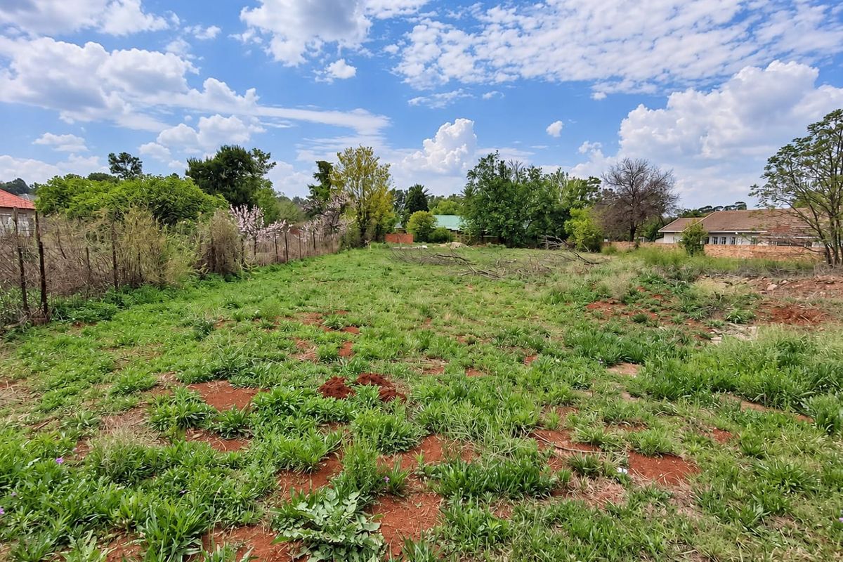 A vacant residential plot featuring natural grass cover, mature trees, and perimeter wire fencing, offering a clear space for potential development.